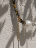 Close-up of Samos braided choker showing charcoal cord with gold and silver chains, free-hanging chain fringe and round freshwater pearl, olive leaf shadows on whitewashed plaster wall, handmade by JLL Pearl