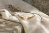 Tama bracelet resting on natural linen cloth on stone, cream round pearl with gold macramé and flower spacers, natural Mediterranean light