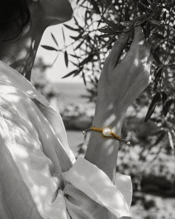 Tama bracelet — round freshwater pearl and gold macramé on wrist, olive branch background, black and white photograph with selective colour on bracelet