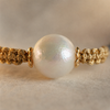 Close-up of Tama bracelet central pearl — 13-14mm round freshwater pearl with iridescent nacre, small gold flower spacers on each side, gold macramé sections
