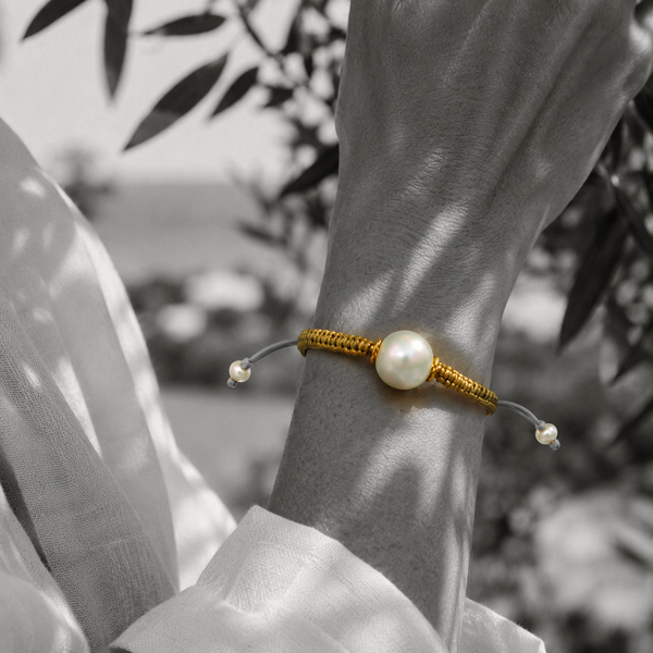 Black and white portrait of a round pearl bracelet on gold macramé cord in an olive grove — JLL Pearl