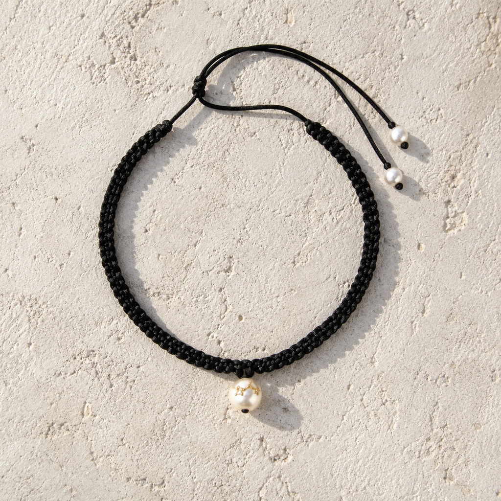 Tara freshwater pearl macramé choker necklace laid flat on pale stone, black hand-braided satin macramé cord, single white pearl with three gold-plated stars, lasso cord with two pearl stoppers, handmade by JLL Pearl