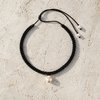 Tara freshwater pearl macramé choker necklace laid flat on pale stone, black hand-braided satin macramé cord, single white pearl with three gold-plated stars, lasso cord with two pearl stoppers, handmade by JLL Pearl