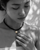 Tara freshwater pearl macramé choker necklace worn by an Asian model, hand resting on pearl with gold stars, dappled leaf shadows on whitewashed wall, B&W with pearl and gold stars in natural colour, handmade by JLL Pearl
