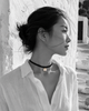 Tara freshwater pearl macramé choker necklace worn in profile by an Asian model against a whitewashed Greek wall, black satin braided cord, pearl with gold stars in natural colour, handmade by JLL Pearl