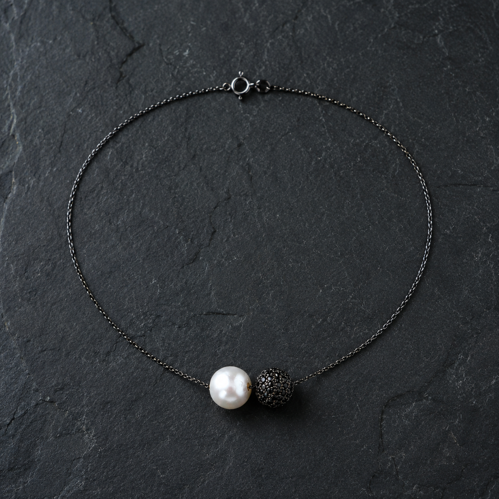 Zephyr pearl necklace black spinel oxidized silver flatlay on dark slate, round white freshwater pearl and black pavé spinel sphere side by side, spring ring clasp visible