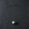 Zephyr pearl necklace black spinel oxidized silver flatlay on dark slate, round white freshwater pearl and black pavé spinel sphere side by side, spring ring clasp visible