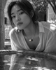 Zephyr pearl necklace black spinel oxidized silver lifestyle, Asian model leaning over stone fountain in Greek courtyard, necklace reflected in still water