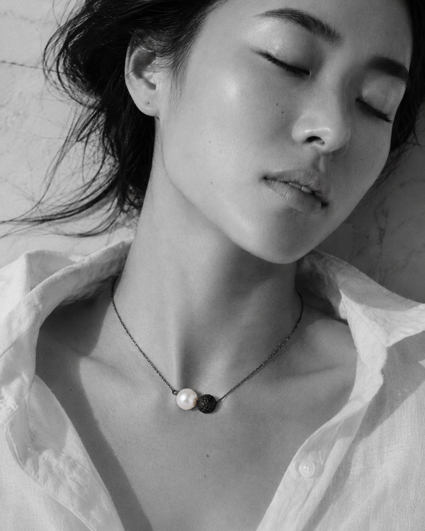 Zephyr pearl necklace black spinel oxidized silver worn by Asian model lying on marble, eyes closed, white linen shirt open, Mediterranean light, handmade by JLL Pearl